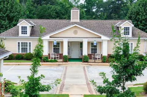 Exterior view of a beige senior living facility with a covered entrance and green landscaping