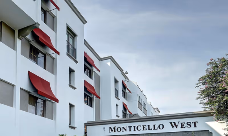 Exterior view of Monticello West building with white walls and red window awnings under a partly cloudy sky.