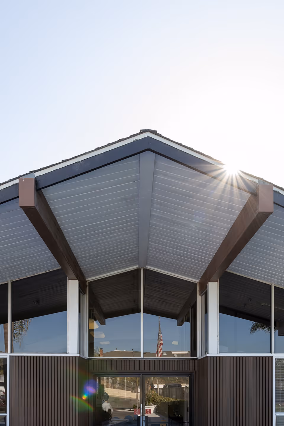 Front facade of a building entry with a pitched roof, large windows, and sun glare near the roofline.