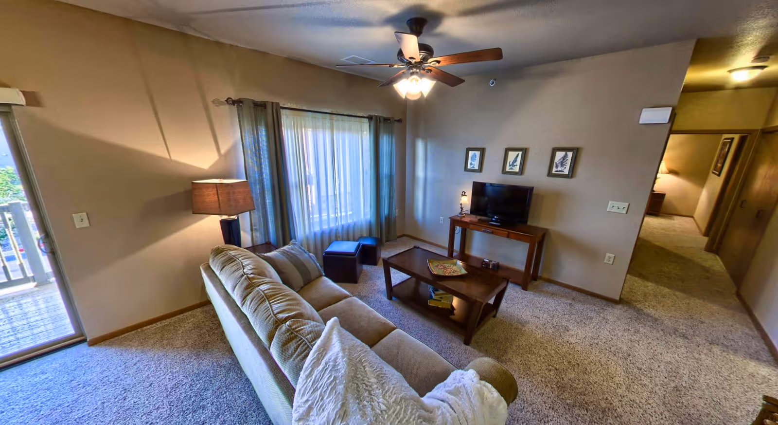 Cozy living room with a sofa, coffee table, TV on a console, lamp, ceiling fan, and sliding glass door to a balcony.