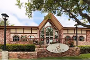Front exterior of a brick senior living facility with arched windows, landscaping, and a stone sign that says "Victoria".