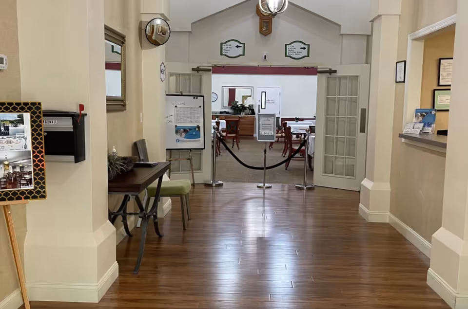 Hallway lobby leading to an open dining room with tables and chairs visible through double doors and a rope barrier.