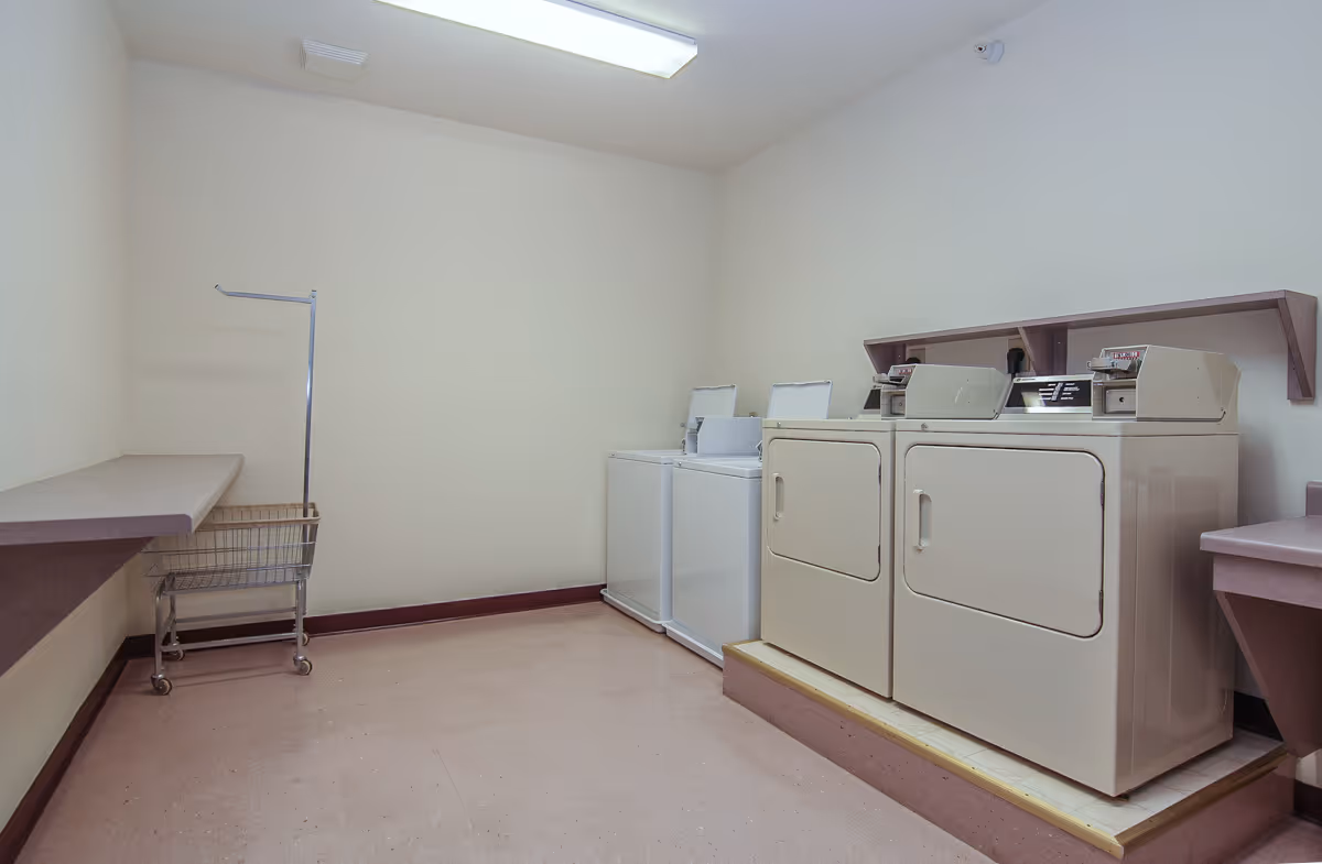 A small laundry room with coin-operated washers and dryers, a folding counter, and a laundry cart.