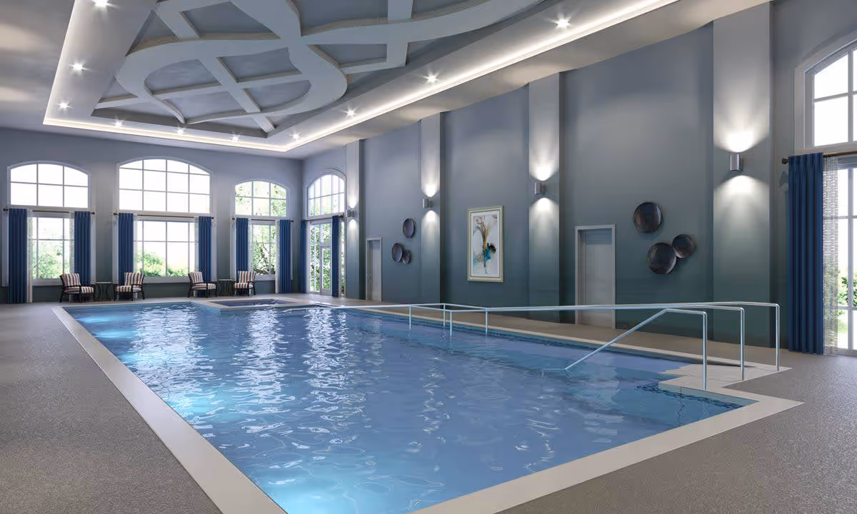 Indoor swimming pool in a spacious, high‑ceiling room with large windows, lounge chairs, and handrails.