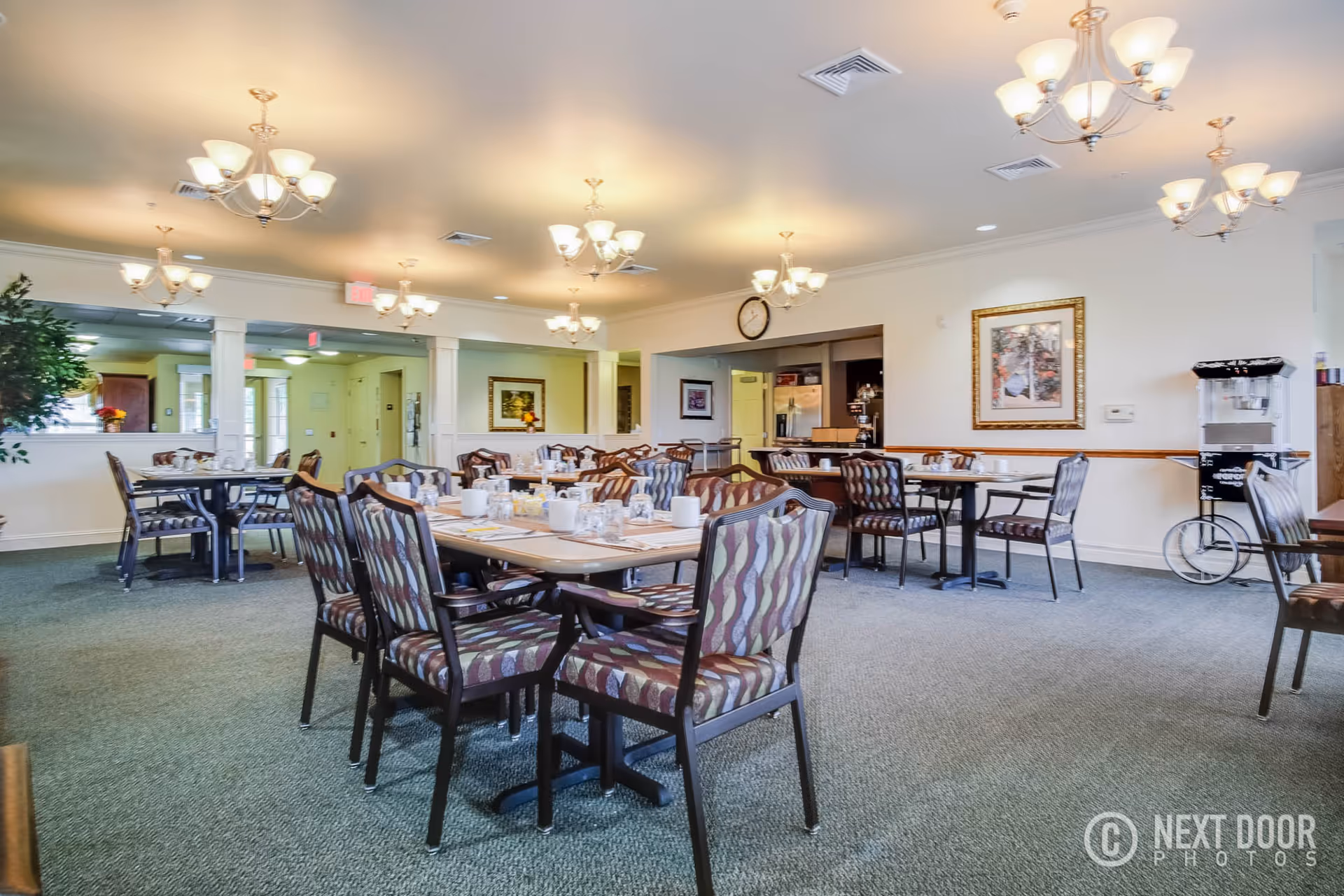 Bright retirement community dining room with multiple set tables and chairs under chandeliers.