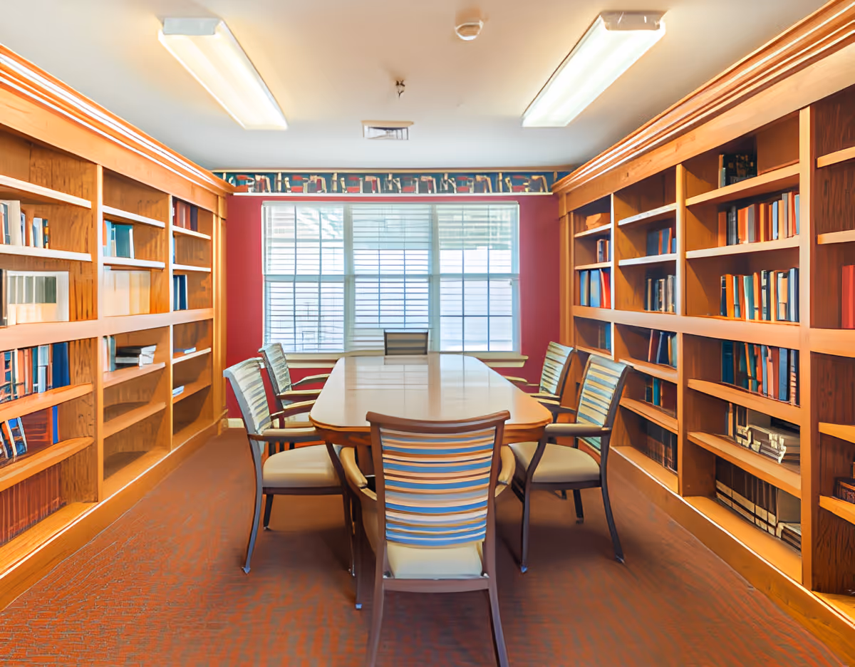 A meeting-style library room with a long table surrounded by chairs and bookshelves lining both walls.