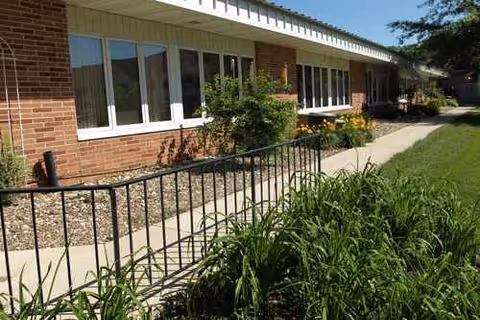 Brick exterior of NewAldaya Lifescapes with windows, walkway, railing, and landscaping.