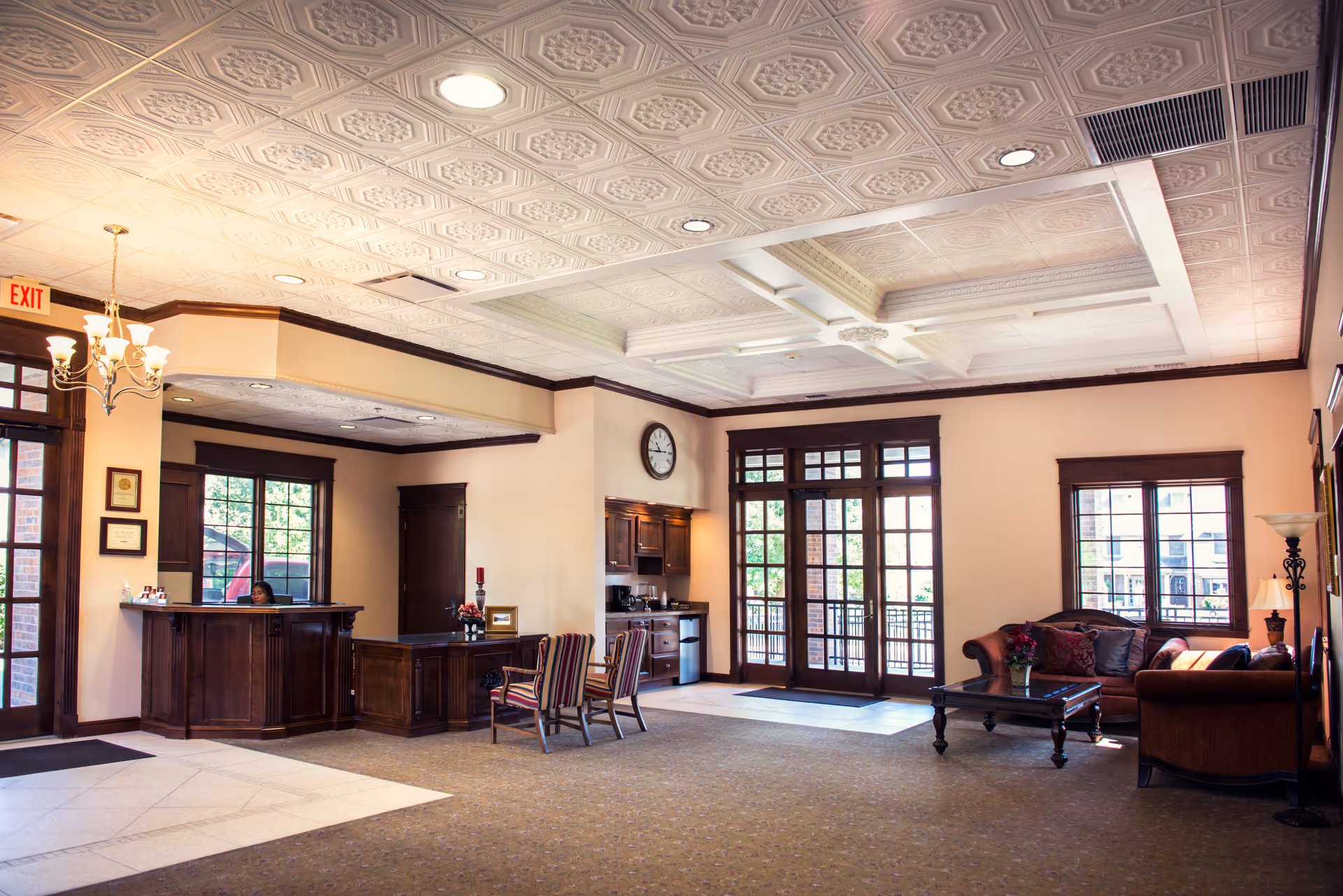 Spacious, well-lit reception lobby with a wooden front desk, seating area, and decorative coffered ceiling.