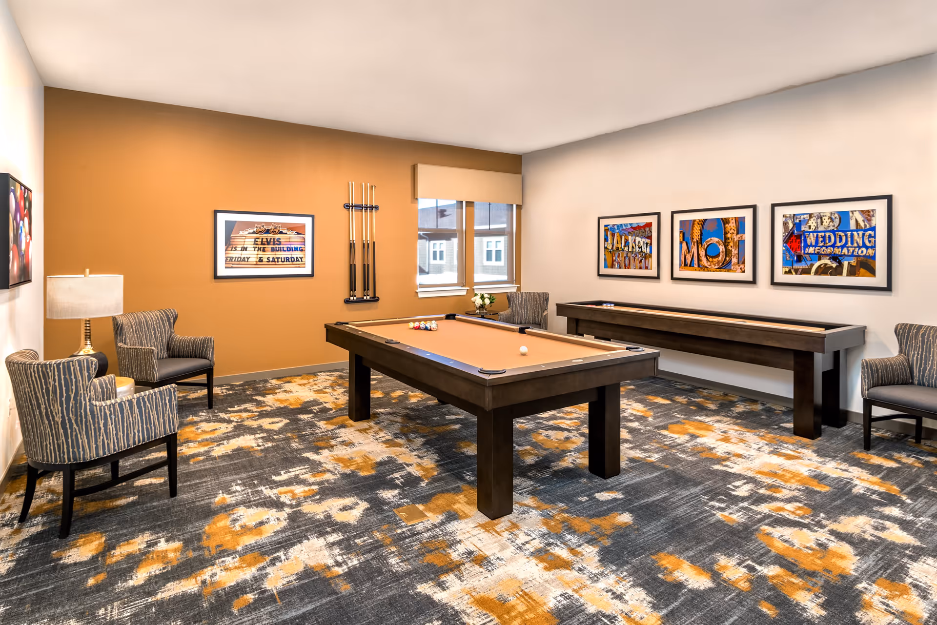 Bright game room with a pool table and shuffleboard, patterned carpet, seating, and framed artwork on the walls.