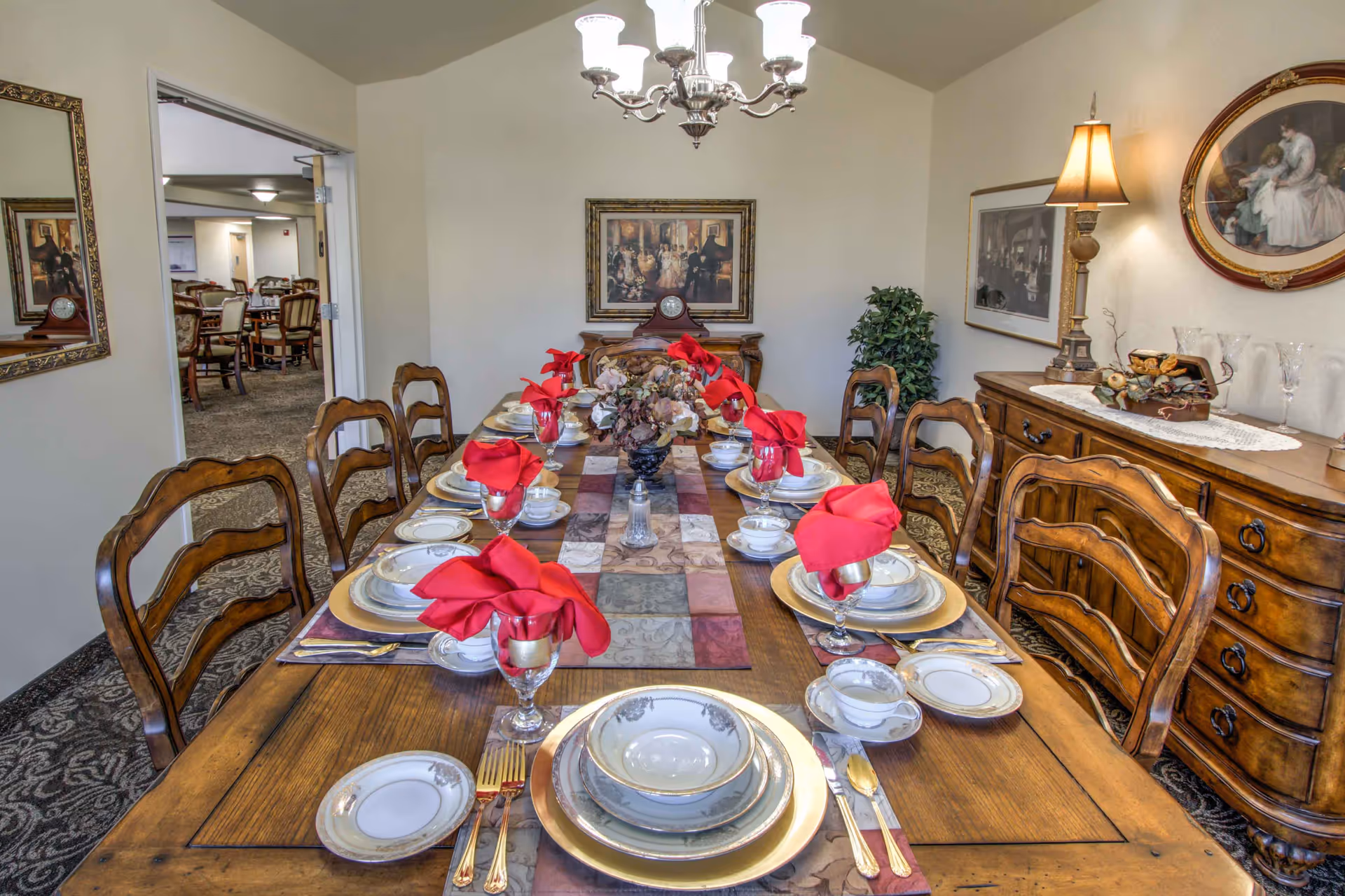 Formal dining room with a long wooden table set with china, red napkins, and wooden chairs in a decorated interior.
