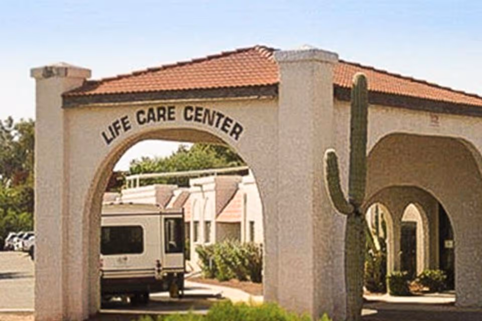 Arched entrance to the Life Care Center with a tiled roof, a tall cactus, and a vehicle parked beneath the arch.