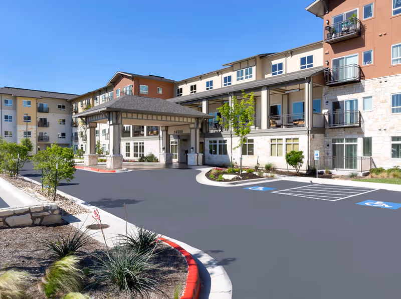 Front entrance of a multi-story senior living building with a covered porte-cochere, landscaped driveway, and handicap parking spaces.