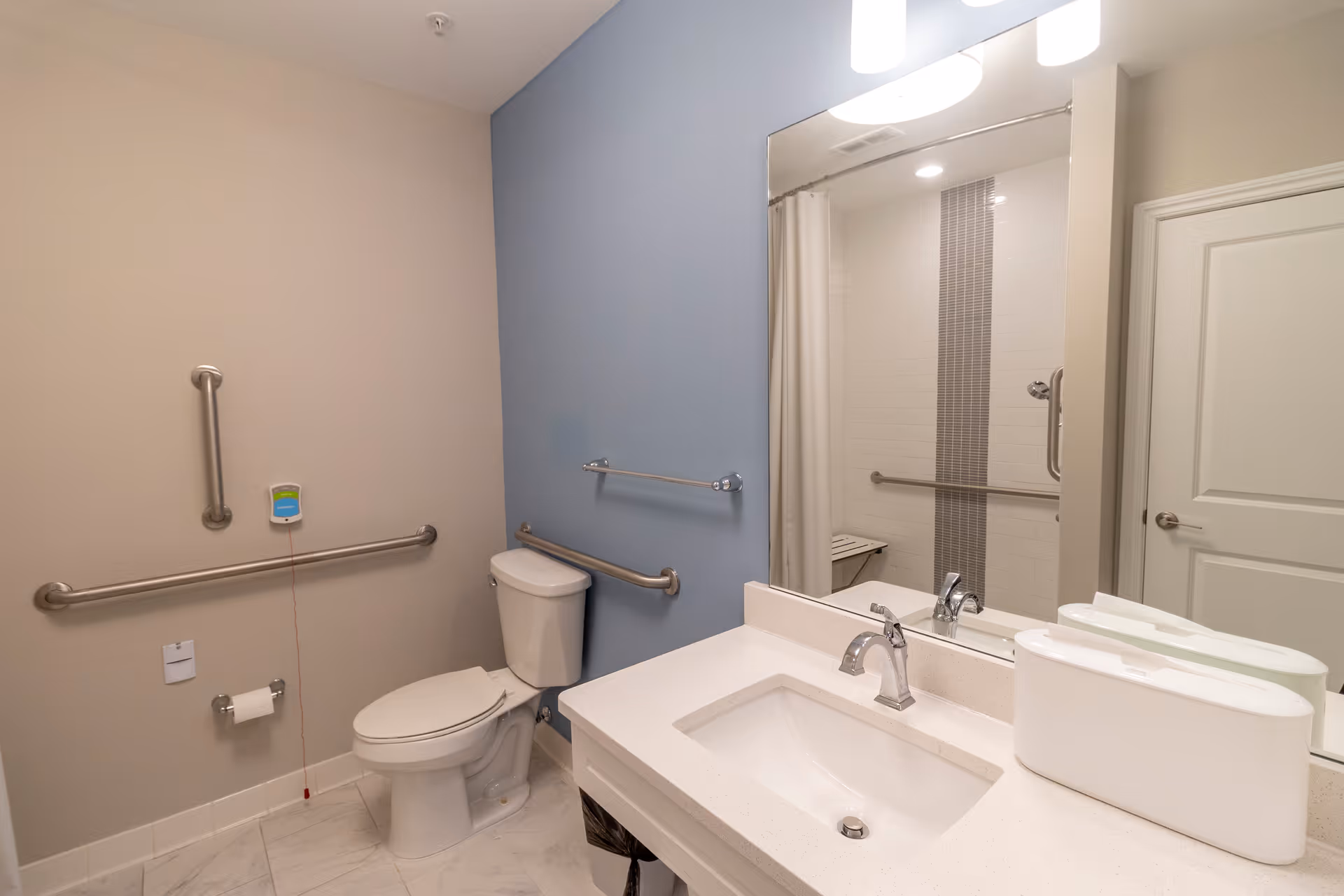 Accessible bathroom with a toilet, countertop sink and mirror, grab bars, and a shower with a curtain.