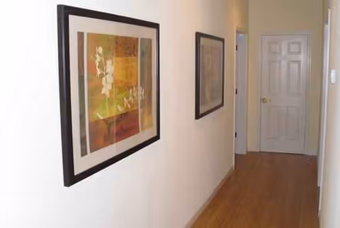 Interior hallway of a care home with framed artwork on white walls and a wooden floor.