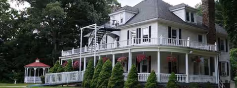 Two-story white building with wraparound porch and hanging flower baskets.