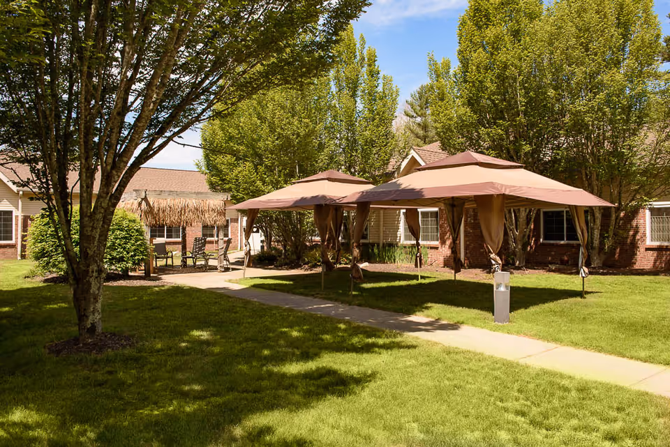 Sunny courtyard at The Oaks with canopy tents, patio seating, trees, and a walkway in front of brick residential buildings.