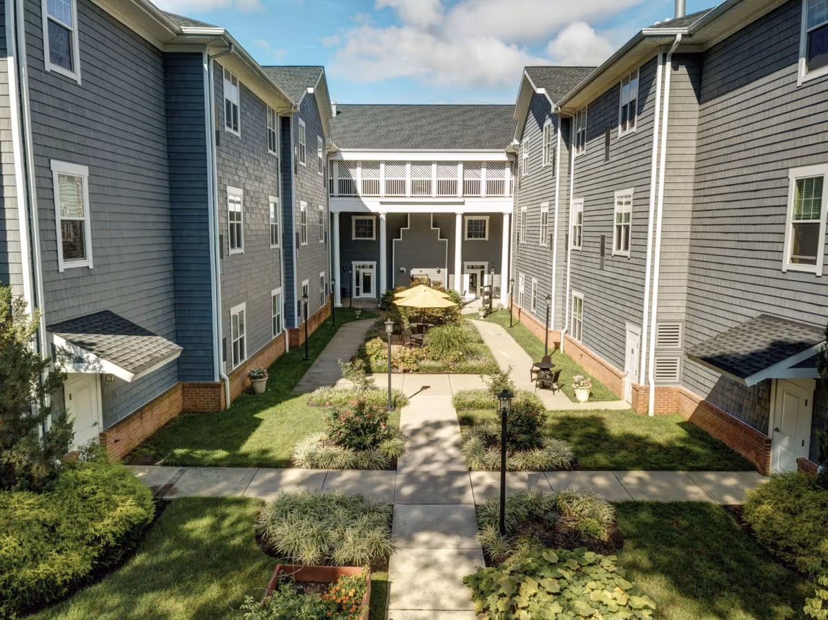 Central courtyard with walkways, landscaping, and seating between two three-story gray-sided buildings at Symphony Manor.