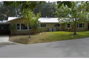 A single-story senior living facility exterior with a grassy lawn, trees, and a driveway.