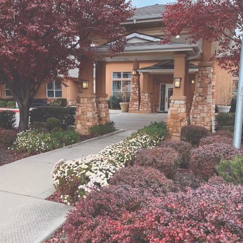 Entrance to Emerson House at River Pointe featuring stone columns, walkway, and landscaped shrubs.