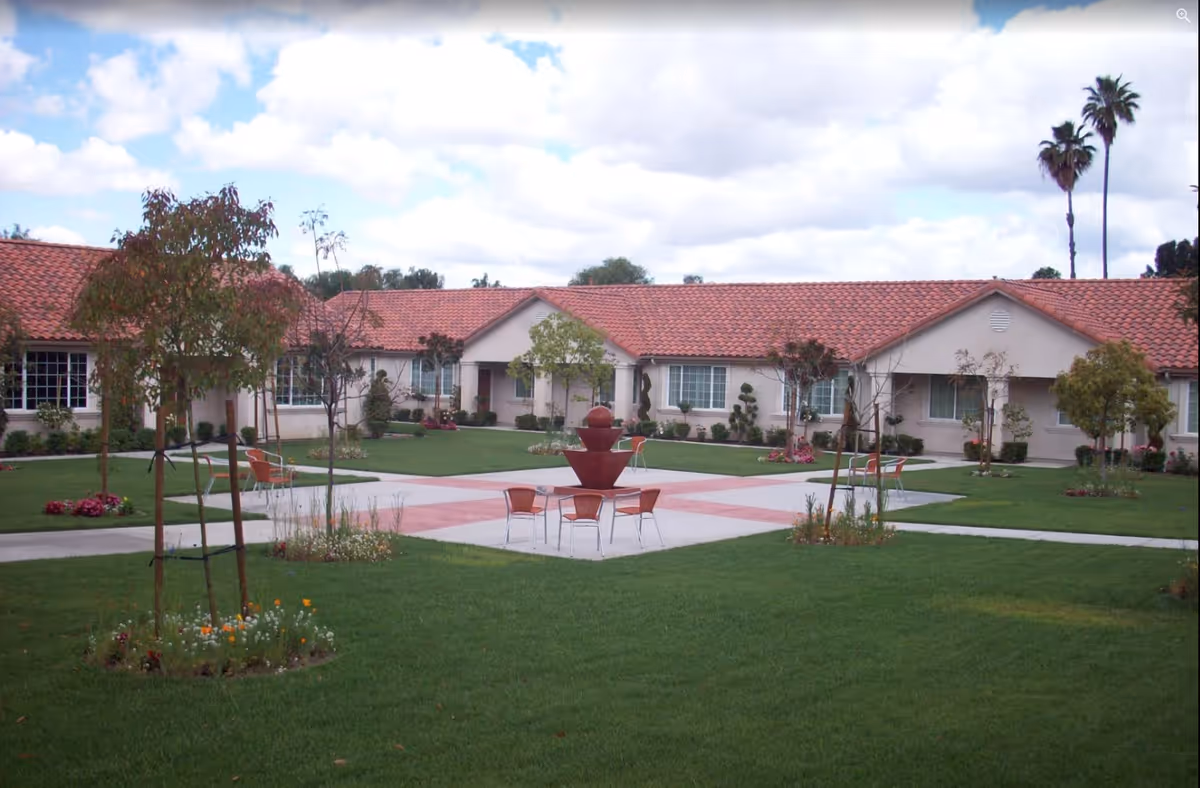 Manicured courtyard with a central fountain, patio chairs, green lawns and single-story buildings with red tile roofs.