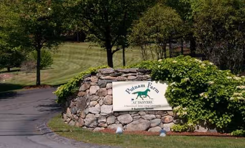 Stone entrance sign for Benchmark Senior Living at Putnam Farm, surrounded by greenery.