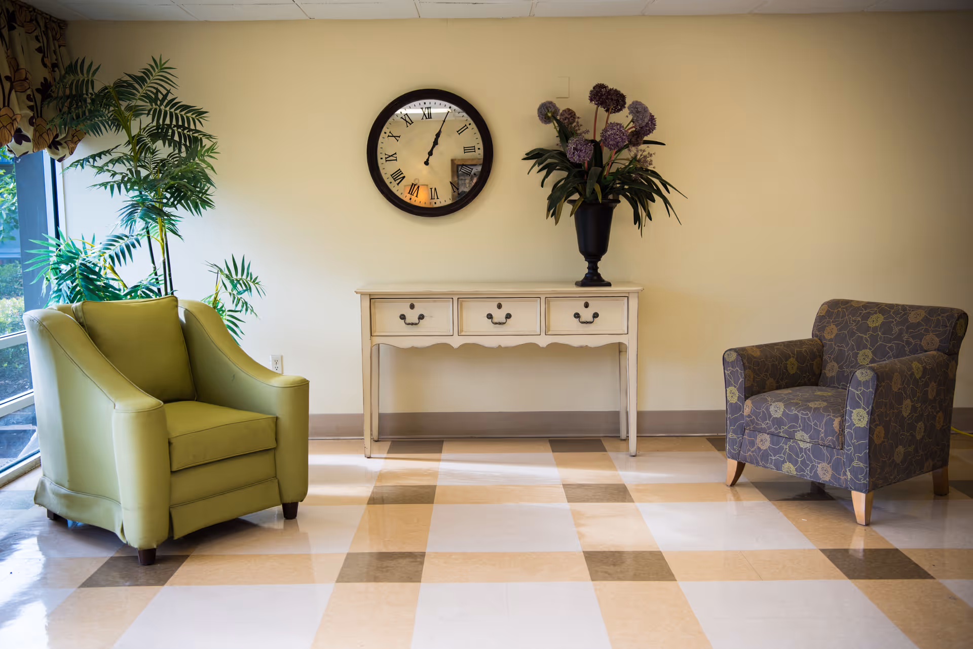 A small seating area with two armchairs flanking a console table topped with a clock and floral arrangement.