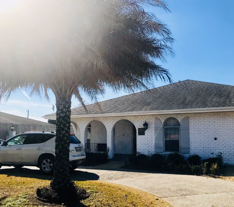 Front view of a white brick senior living facility with arches, palm tree, parked SUV.
