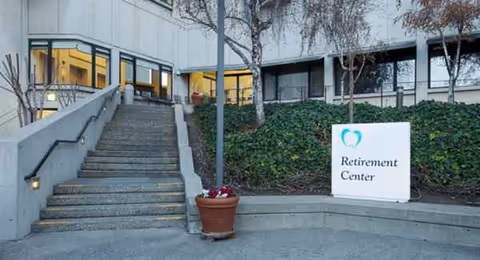 Exterior view of Mercy Retirement & Care Center entrance with steps, glass doors, and sign.