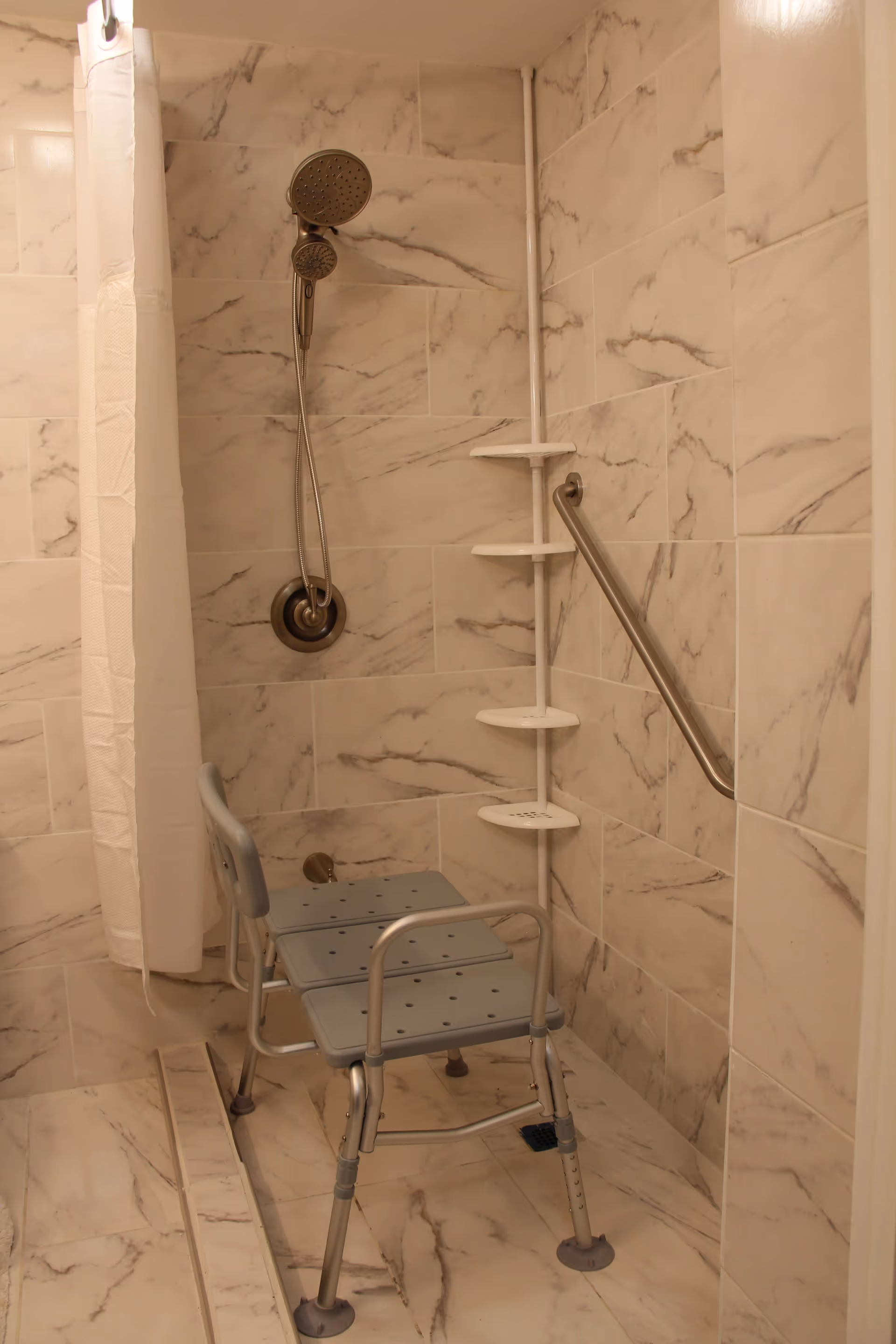 Tiled accessible shower with a handheld showerhead, grab bar, corner shelves, and a shower chair.
