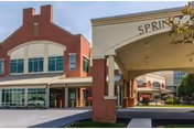 Exterior view of the Spring Creek facility showing a brick building with large windows and a covered entrance with the name 'Spring Creek' displayed on the archway.