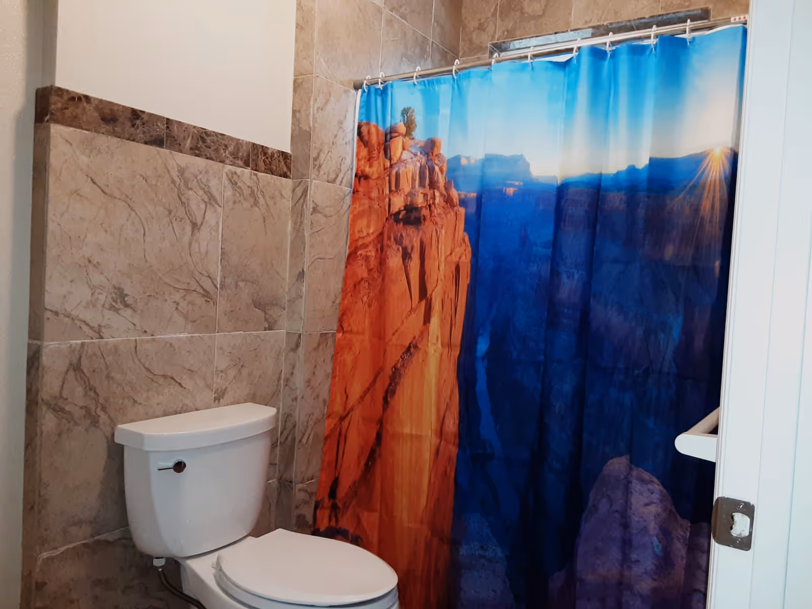Small bathroom with a toilet and a shower featuring a canyon-themed shower curtain and tiled walls.