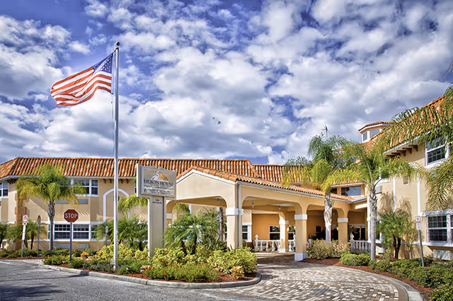 Heron House Assisted Living front entrance with flagpoles and palm trees.