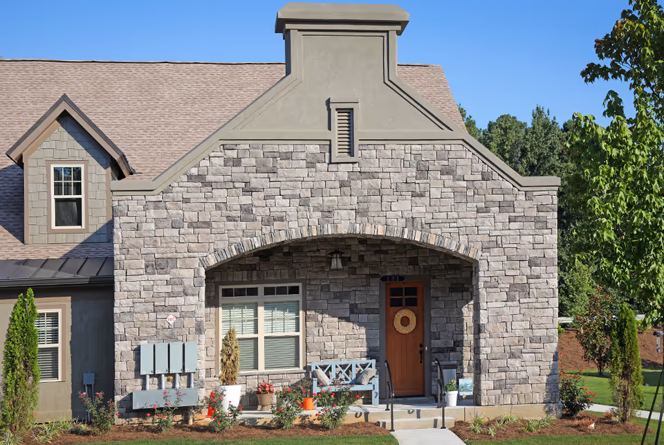 Stone-front building facade with a small covered porch, wooden door, window and landscaped front yard.