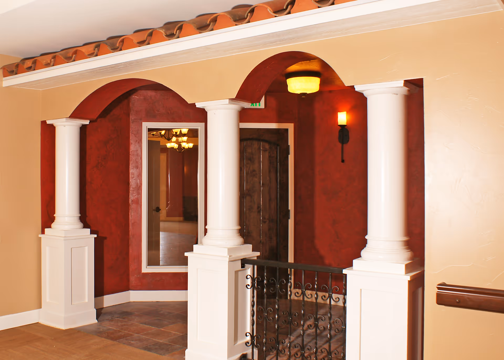 Interior entryway with white columns, arched openings, red textured walls, and a decorative wrought-iron railing.