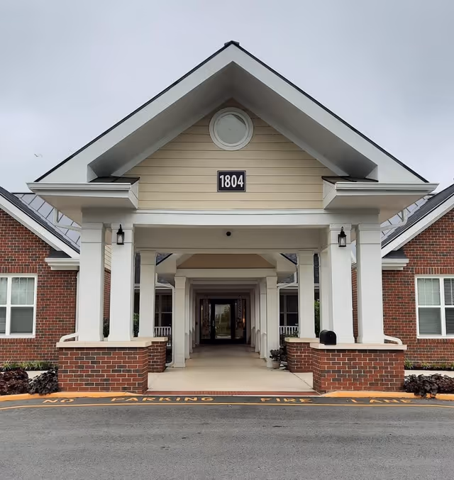 Front entrance of a brick senior living facility with white columns and walkway.
