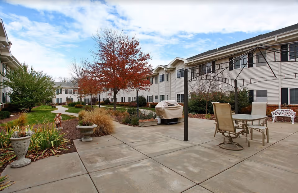 Outdoor courtyard between two-story assisted living buildings with patio seating, planters, and a paved walkway.