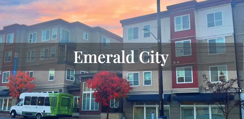 Exterior view of Emerald City at Greenlake Senior Living building with a shuttle van and trees.