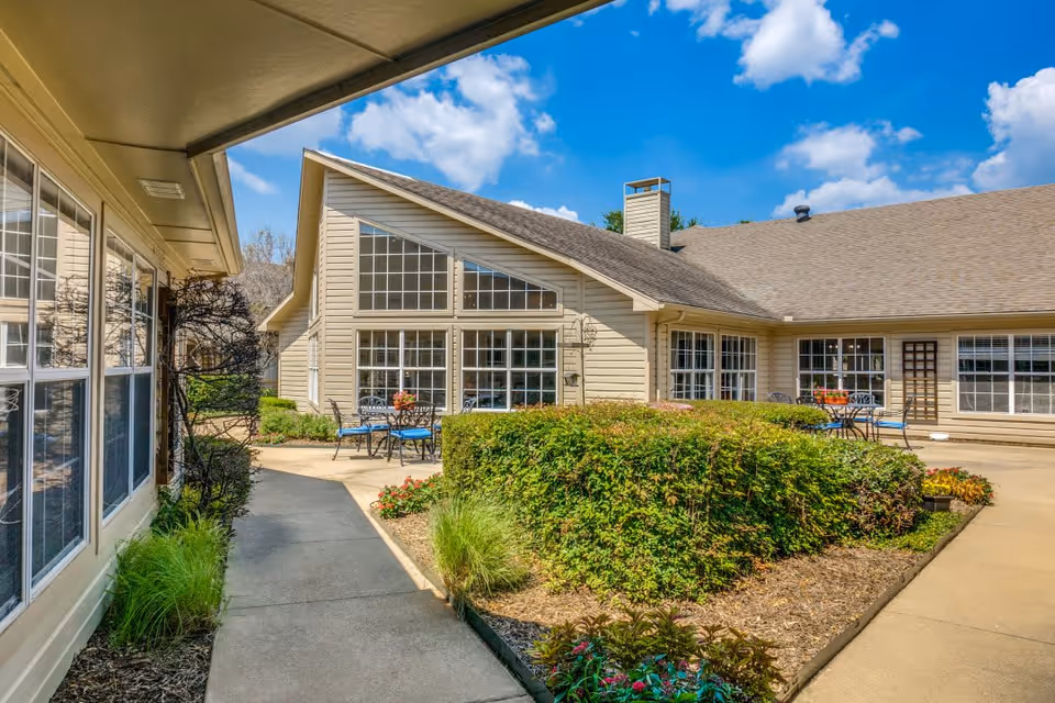 Exterior view of Anointed Senior Living showing a landscaped pathway leading to the building with large windows and outdoor seating.