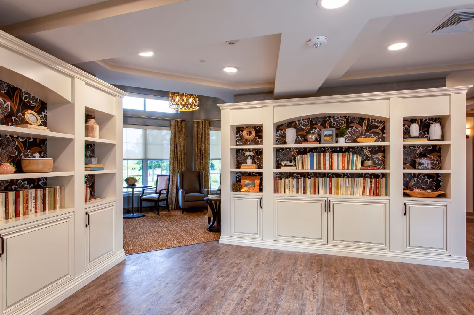 Bright communal lounge with built-in white bookshelves, decorative items, and seating by a large window.