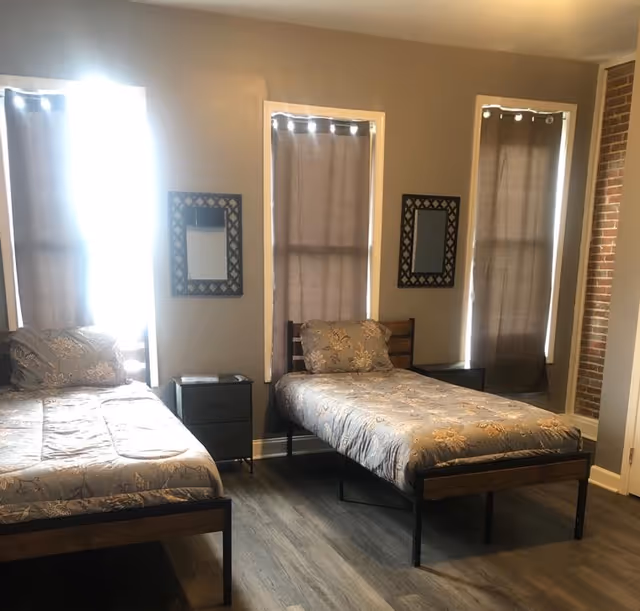 Two single beds with matching bedding and a nightstand in a shared, window-lit bedroom.