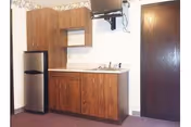 Small kitchenette with wood cabinets, a mini refrigerator, sink, wall-mounted TV, and a closed wooden door.
