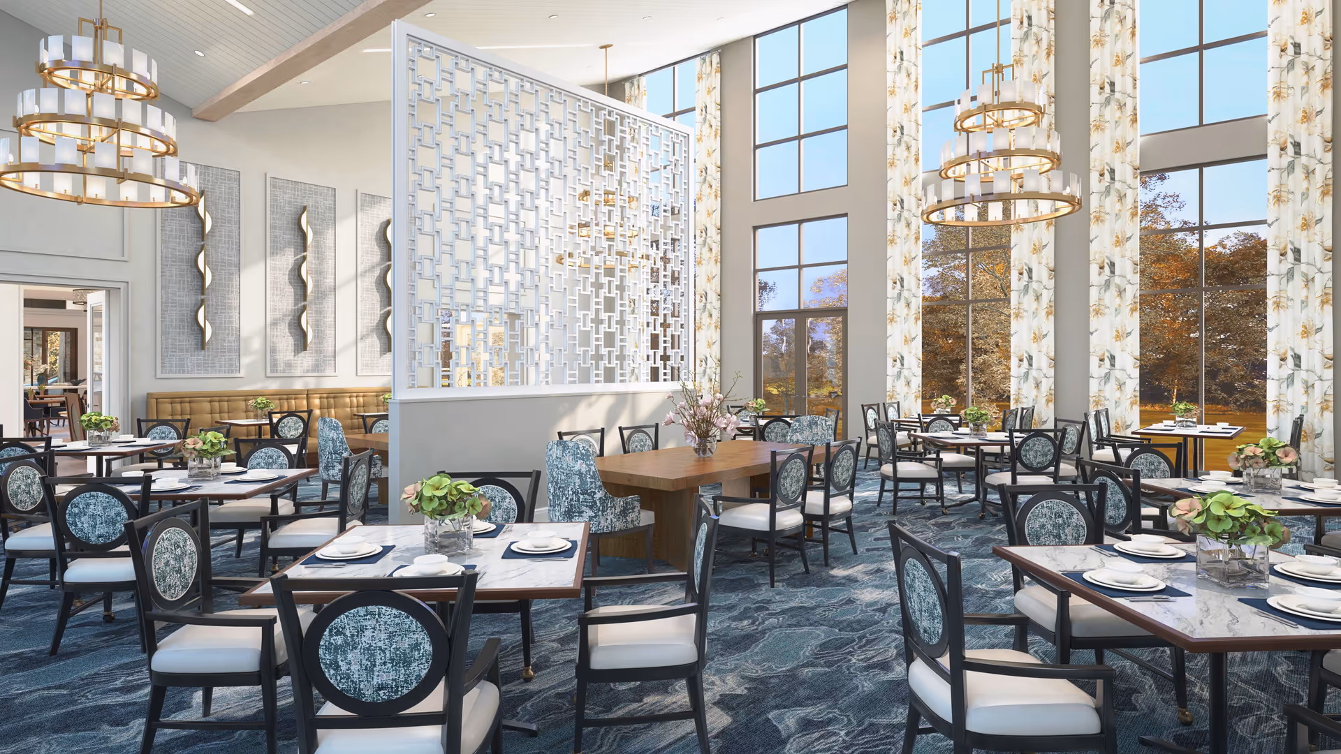 Spacious, elegant dining room with numerous set tables and chairs, large windows with floral curtains, a decorative room divider and chandeliers.