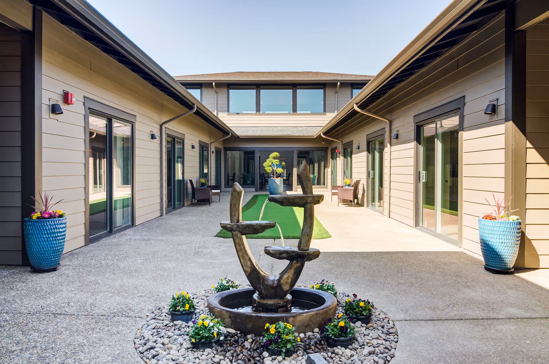 Sunny enclosed courtyard with a tiered fountain, potted plants, and sliding glass doors leading to rooms.