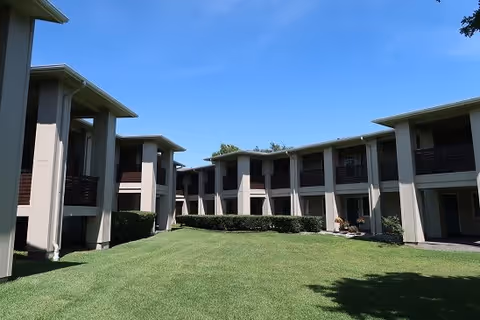 Two-story U-shaped apartment building with balconies surrounding a well-kept grassy courtyard under a clear blue sky.