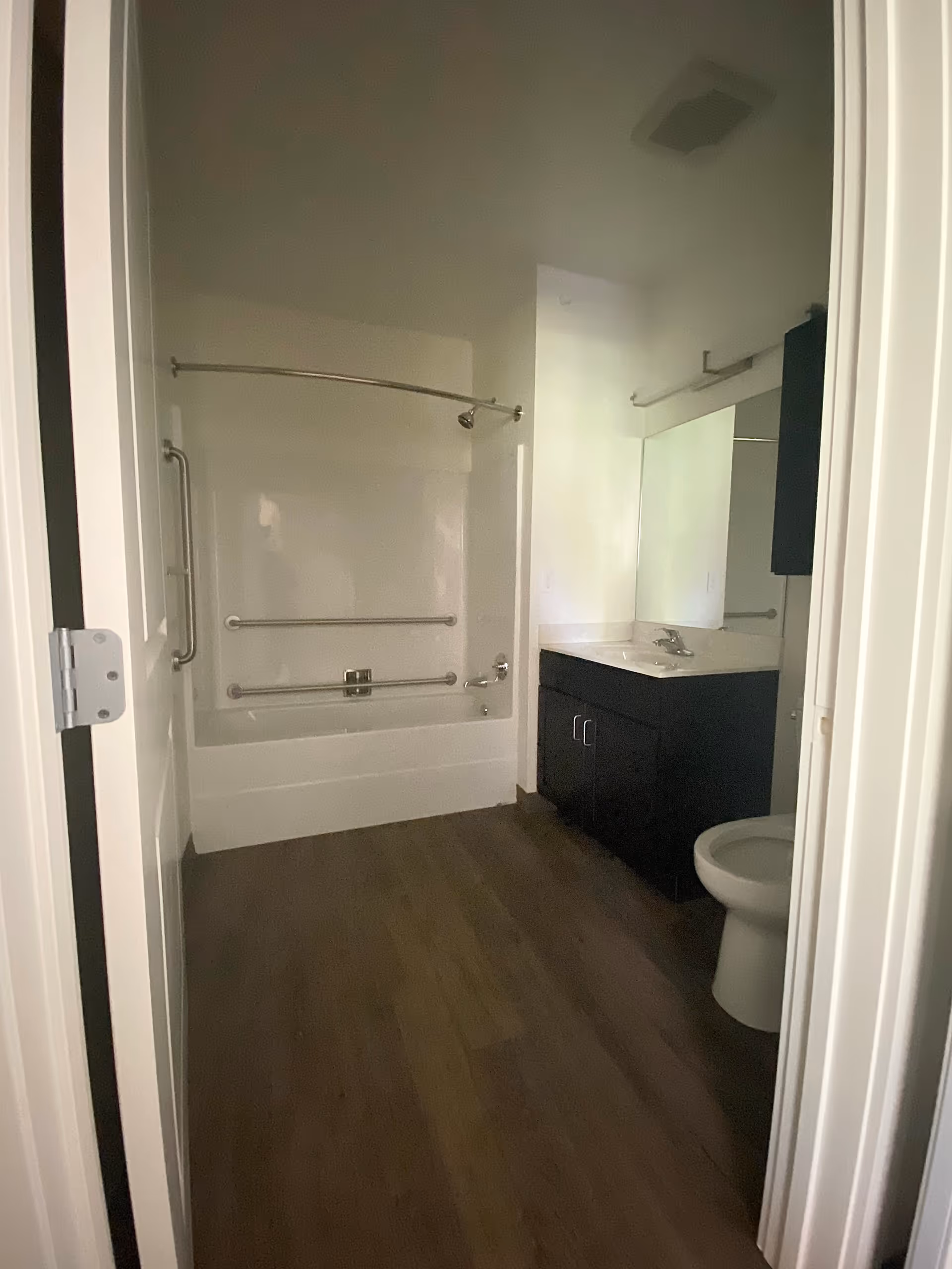 Interior view of a bathroom showing a bathtub/shower with grab bars, a vanity with sink and mirror, and a toilet.
