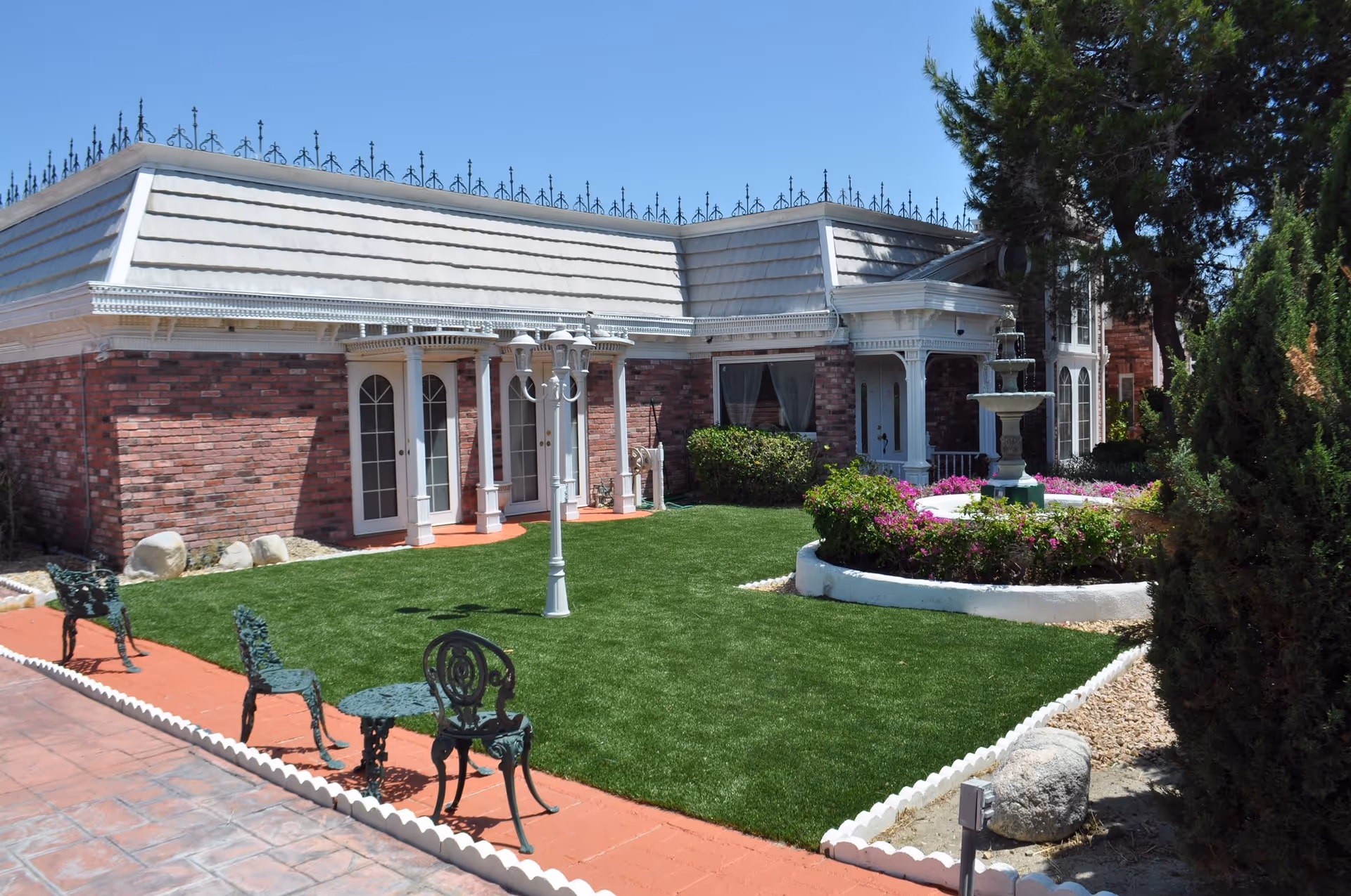 Front courtyard of a brick senior living facility featuring a manicured lawn, fountain, lamppost, and outdoor seating.