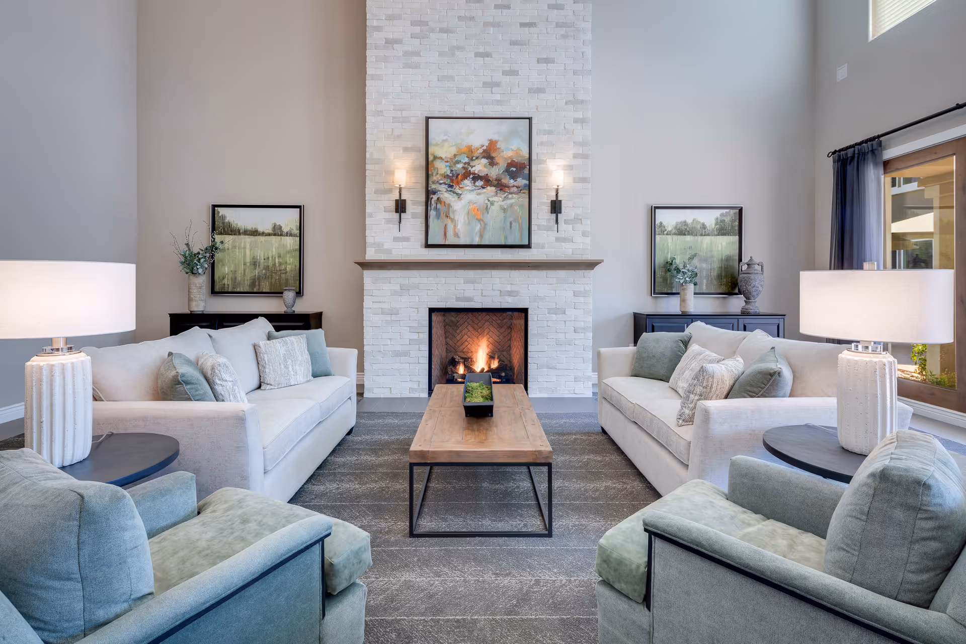 Bright modern living room with two sofas and armchairs arranged around a wooden coffee table in front of a lit fireplace and artwork.