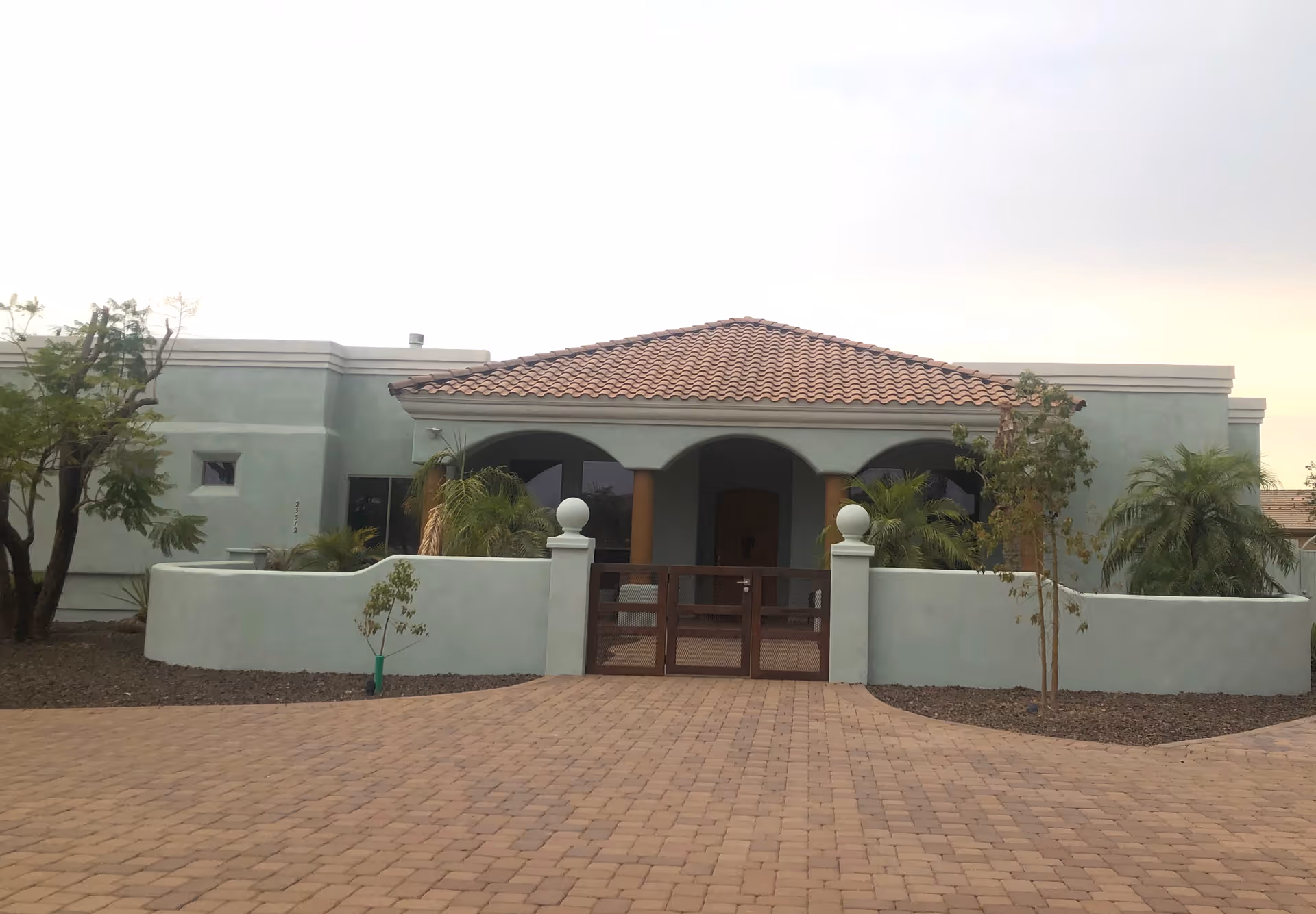 Front exterior of a single-story stucco building with a tiled roof, gated entrance, and paved driveway.