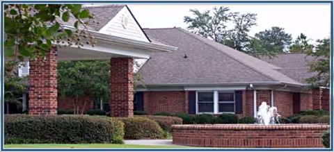 Brick senior living facility exterior with a covered entrance, fountain, and manicured landscaping.