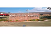 Brick entrance sign reading 'SONGBIRD LODGE' with landscaping, an American flag, and the facility building visible behind it.
